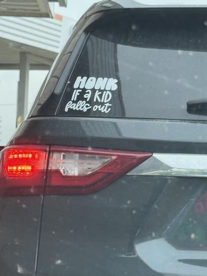 SUV with sticker in rear window that says “honk if a kid falls out.”