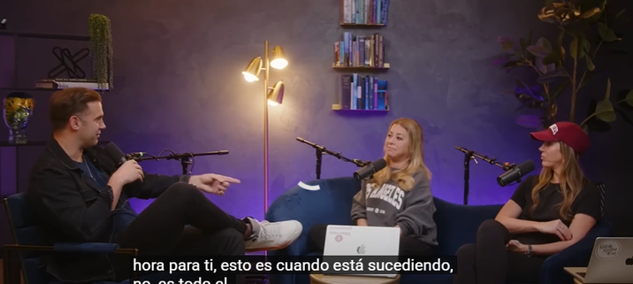 Tres personas sentadas en un estudio de grabación conversando, con micrófonos y pantallas de computadora visibles.