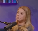 Una mujer con cabello largo y rubio, sentada frente a un micrófono, con una expresión de preocupación mientras parece reflexionar sobre una conversación.