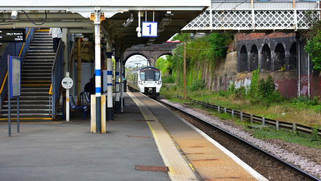 A passenger train approaches a mostly empty outer platform at a small station, on which a staircase and a covered waiting area are visible on the left.

Ein Personenzug naehert sich an einer kleinen Station einem ueberwiegend leeren Aussenbahnsteig, auf dem links eine Treppe und ein ueberdachter Wartebereich zu sehen sind.