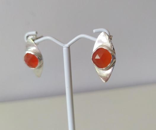 a pair of silver romboid stud earrings with an orange gemstone each. They are hanged on white wire