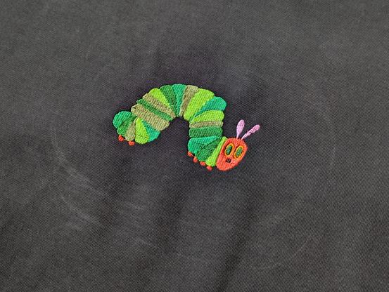 Nahaufnahme von einer kleinen Raupe Nimmersatt, die von einer Maschine auf Textil gestickt wurde.