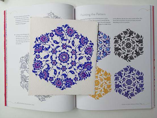 The same pattern from picture 1, above a book opened to show the instruction pages from the book in picture 3 for creating that pattern. On the right-hand page are four versions of the pattern, one in ultramarine and cyan, and then three monocolored versions, in black, ochre, and ultramarine.