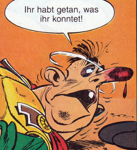 Ein farbiger Comic-Ausschnitt in Nahaufnahme. Im Bild ist der Kopf und Oberkörper eines angeschlagenen Mannes mit zerschundenem Gesicht zu sehen. Er trägt eine gelb-grüne Tunika mit rotem Umhang und goldener Brosche. Seine Nase ist stark gerötet und blutet, ein Auge ist blau geschlagen. Er blickt mit weit aufgerissenen Augen und geöffnetem Mund zur Seite. Der Hintergrund ist orange. Er sagt: „Ihr habt getan, was ihr konntet!“