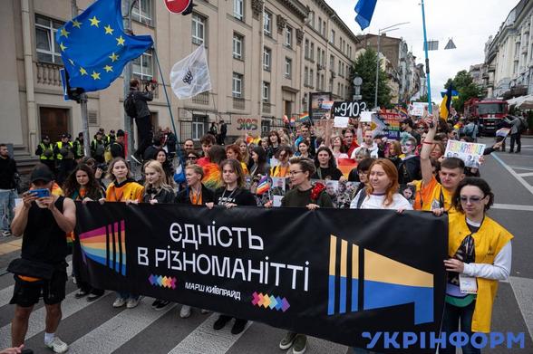 A group of people on a pride march with a sign in Ukrainian, "єдність в Різноманітті" which translates as unity in diversity. There is an EU flag flying.
