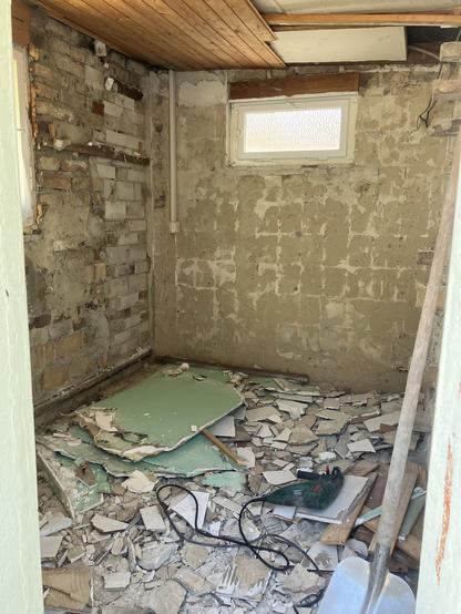 Foto eines völlig zerstörten und mit Schutt überhäuften Bades; im Schutt liegt ein Bosch Bohrhammer und an der rechten vorderen Seite steht eine Schauf; selbst Teile der Deckenverkleidung fehlen