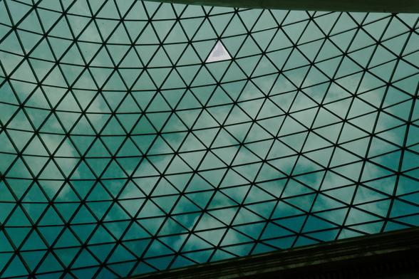 Vertical photo of the British Museum ceiling with one transparent triangle visible and clouds in the background.