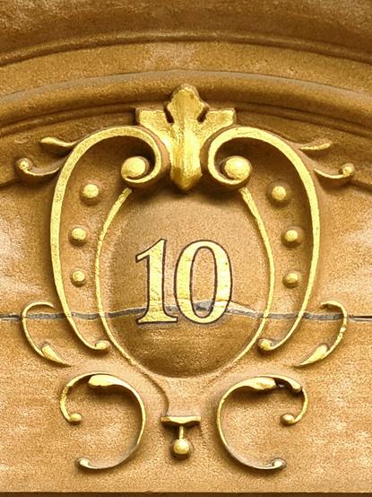 A house number hand-painted in gold paint on a sculpted cartouche on an Edwardian townhouse in Glasgow.