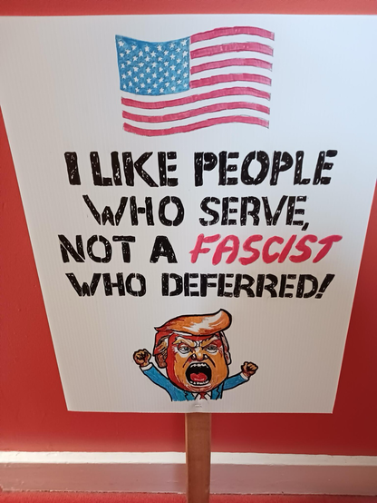 Sign saying “I like people who serve, not a fascist who deferred” with a flag and a picture of Trump being a baby