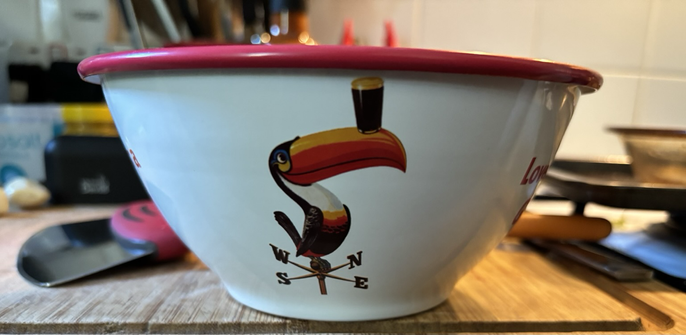 An enamelled bowl sporting various vintage Guinness motifs. This side being a toucan on a weathervane with a pint balanced on its beak.