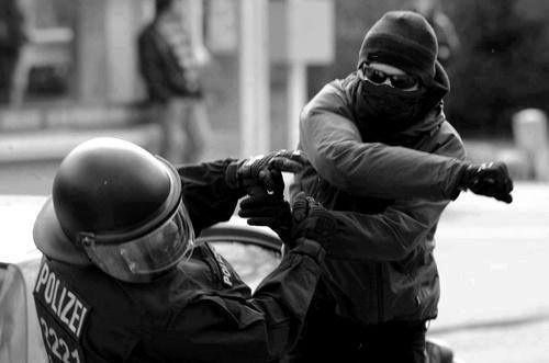 Black and white photograph of an masked and gloved individual beating the fuck out of a german riot cop.