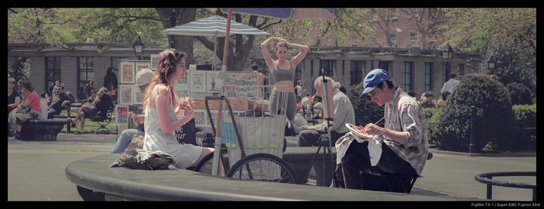 A person sits on a stone bench in front of another person, who has an easel in front of them and a paint plate in one hand.  Washington Square Park is visible in the background.