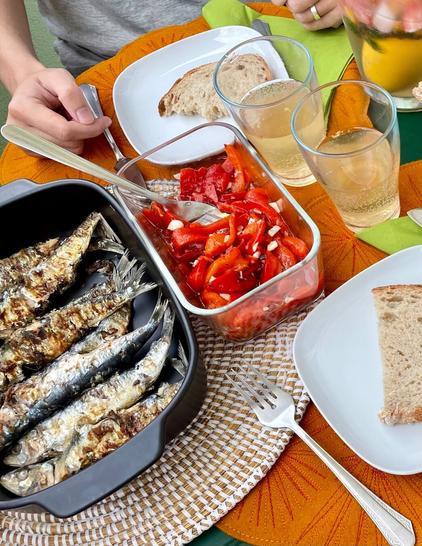Table view from above with grilled sardines, bread and red pepper. White sangria jar and orange placemats for two.