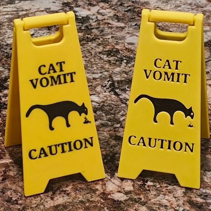 two yellow placards that say "cat vomit - caution" with a stylized cat throwing up