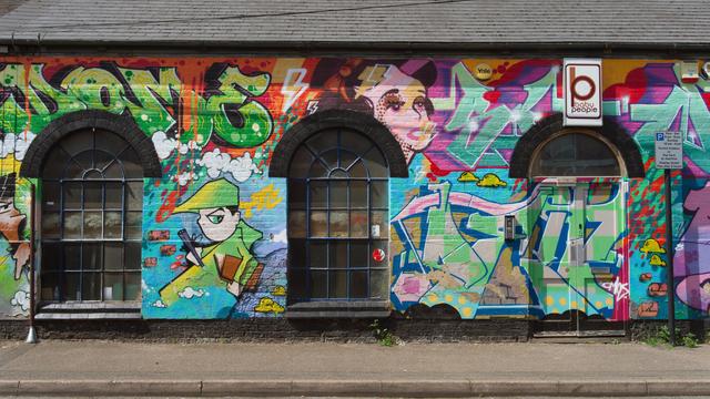 A single story warehouse converted into a recording studio has a colourful wall of graffiti style artwork covering it's wall and door.