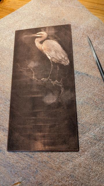 Photo of a copper plate that has been roughened for mezzotint, being worked on with a scraper, that is shown next to it. The image on the plate is an egret perched on a branch.