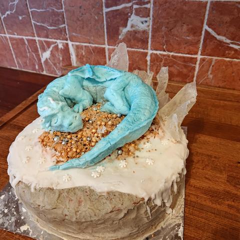 A cake topped with an ice blue dragon, sleeping on a little pile of treasure. Behind it are ice shards stuck into the cake, pointing up. The shards are cloudy now, like quartz.