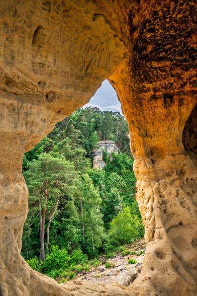 Sandstein Kammer mit natürlichem Fenster nach draußen. In der Öffnung ist der grüne Wald zu sehen und weitere Felsformationen