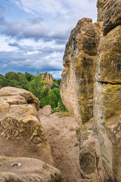Blick durch die Sandstein Formationen. Am Horizont Wolkenhimmel und der Wald und weitere Felsen.