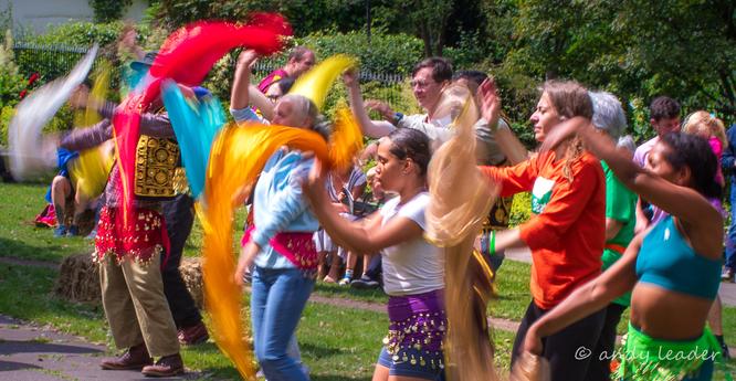 A line of people learning Bollywood dancing. Holding bright colourful scarves which are blurred as they move.