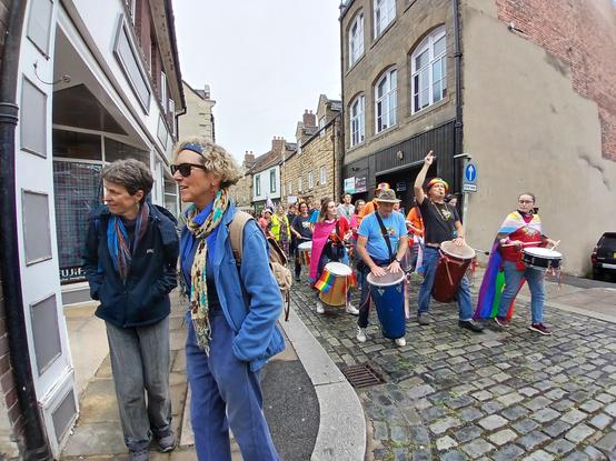 A group of samba drummers wearing pride flags leading a section of the pride March