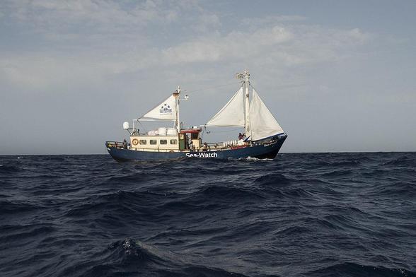 Ein kleiner blauer Kutter mit weißen Aufbauten und drei kleinen Segeln auf hoher See. Auf der Bordwand steht groß Sea-Watch. [Foto: Ruben Neugebauer]
