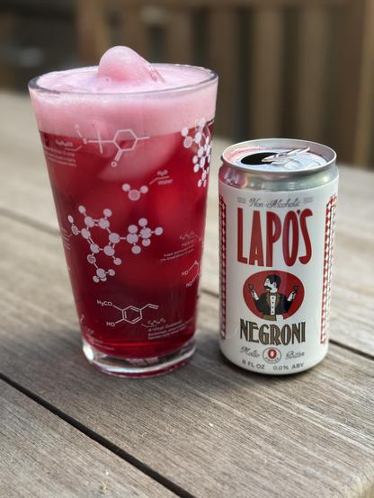 Left, glass of a red fluid with  fizzy top, ice visible. Glass has images of molecules in beer in it. Right, open can. “Non-Alcoholic LAPOS NEGRONI, Molto
Bitter, 8 FLOZ 0.0% ABV”