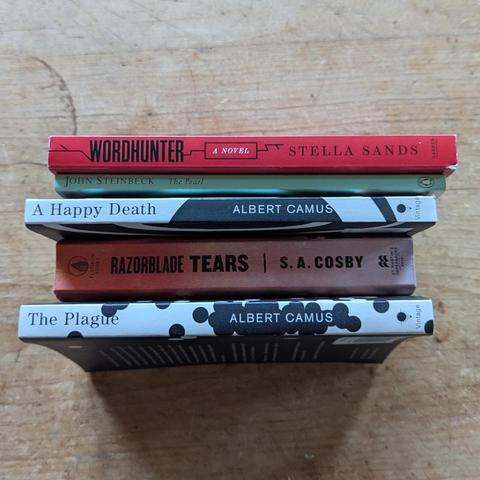 Stack of the spines of five books: Wordhunter by Stella Sands, The Pearl by John Steinbeck, A Happy Death by Albert Camus, Razorblade Tears by S.A. Cosby, and The Plague by Albert Camus