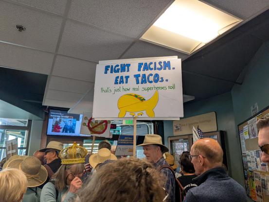 Protesters with sign "fight fascism. Eat tacos. That's how real superheroes roll"