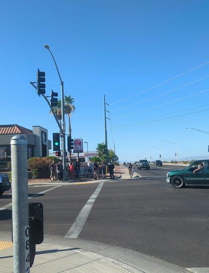 Wide shot of a small group of Trump counter protestors under a Taco Bell sign. Also a green car making a left at the intersection.