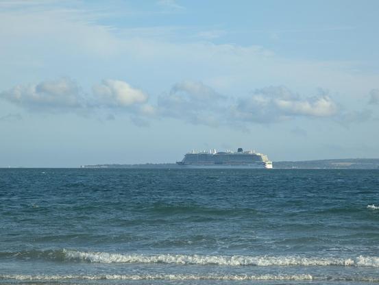 A large cruise ship passing through a wide channel in the evening sunlight