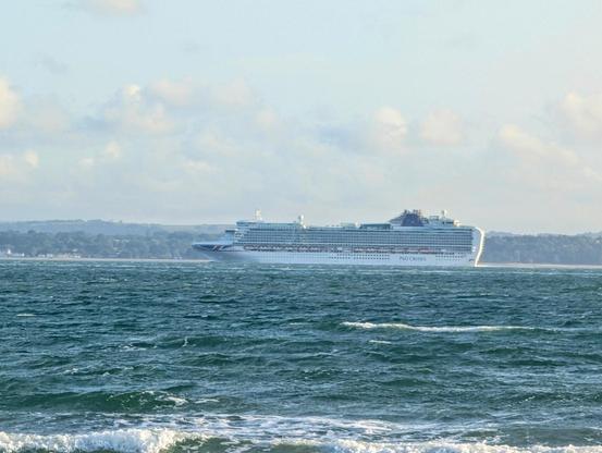 A large white cruise ship on a whitecap flecked sea with a distant landmass behind it