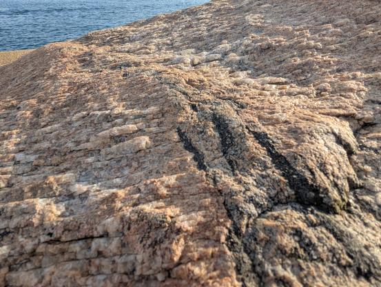 Gros plan sur un rocher granitique en bord de mer, de couleur gris-rose et de texture à la fois ridée avec des espèces de strates granuleuses qui se chevauchent