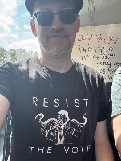 Me wearing a black t-shirt that says “resist the void” with art of Trump as a Cthulhu-like figure with tentacles and lobster claw hands.