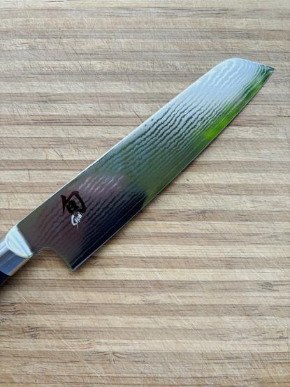 A Shun Classic Master 16.5cm Utility Knife on a well used striped bamboo cutting board.