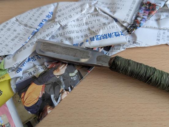 Japanese Kamisori razor on top of some Japanese newspaper and an a table.