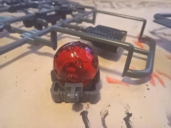 A macro photograph of an HMM Zoid core, a small bumpy PVC orb, translucent red in colour, sitting in the unique command wolf core caddy. It's Good Boy.