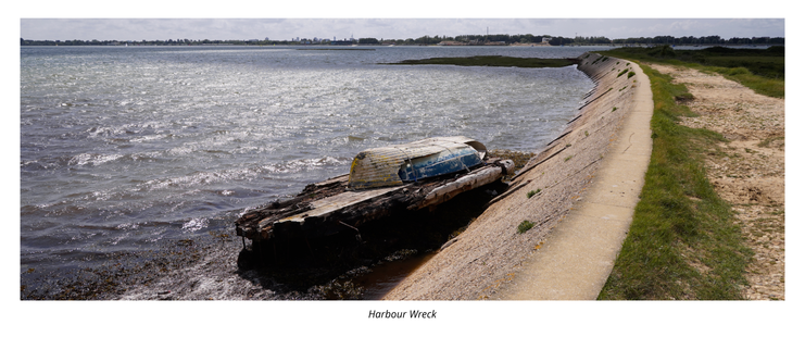 The sea wall stretches off to the horizon. An very old wooden platform has two upside down boats, one within the other, 'bungeed' to the top.