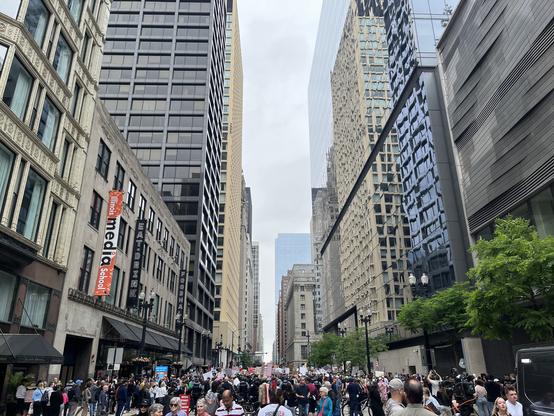 A very large lively crowd of people fill the streets near Chicago Daley Plaza, holding homemade protest signs.