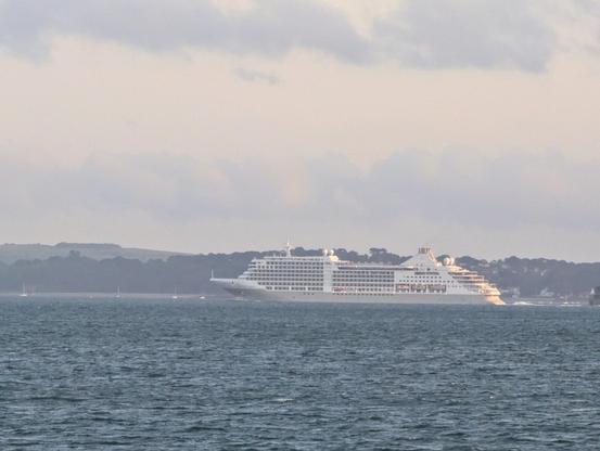 A large white cruise liner at sea with a distant land mass behind it