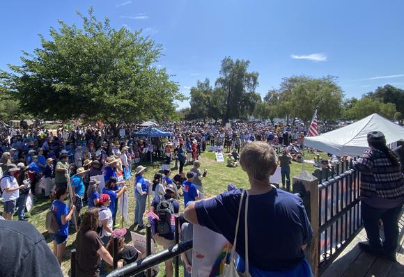 A crowd of patriots gathers in a park in Escondido, CA to march for democracy after listening to speakers and singing This Land Is Your Land as a group.
