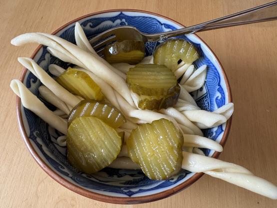 A bowl of pasta with bread and butter pickles on top.