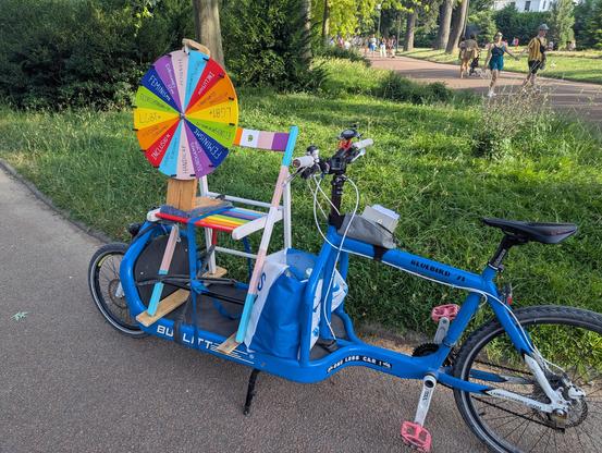 On voit un vélo cargo sur lequel la chaise du pouet précédent est fixée (sur la plateforme avant), et la roue (voir le lien dans le pouêt) est posée dessus, ce qui la met à parfaite hauteur pour jouer