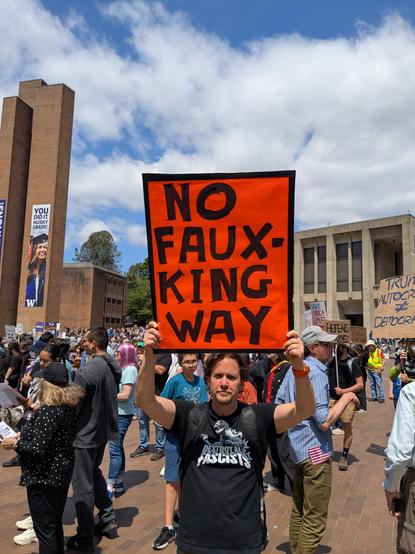 A man at a protest holding a sign that reads "No Faux-King Way"