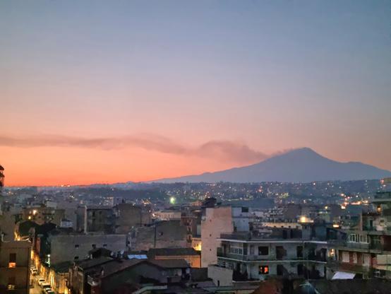 Tra i colori pastello del tramonto, l'Etna fuma, lasciando una lunga scia nel cielo sereno