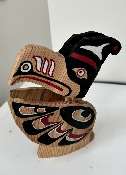 Sculpture of a Thunderbird carved from cedar.  The design colours are black and red with some white highlights.
