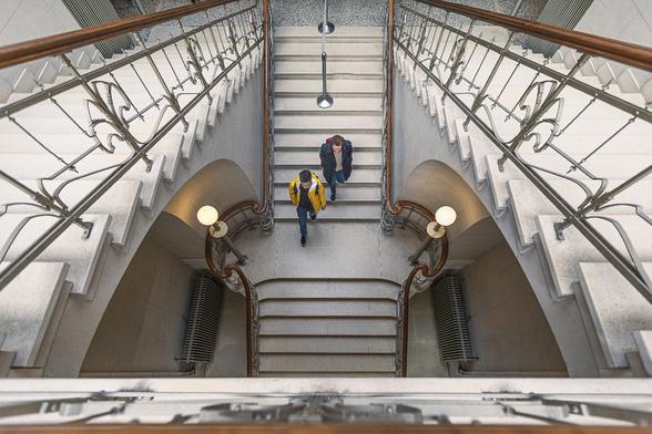 Look-up view symmetrical view of the central split staircases at the Old Waucquez Stores' building in Brussels (now the Comics Museum), by Art Nouveau architect Victor Horta. Two men are descending the stairs, their silhouettes appear rather small on the steps.