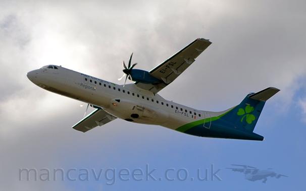 Low side view of a high-winged, twin propellor-engined airliner flying from right to left, with it's undercarriage already tucked away, flaps extended from the rear of the wings, and the nose raised sharply, suggesting it has just taken off.
The plane is mostly white, with green "Aer Lingus" titles on the upper forward fuselage, with grey "Regional" titles below.
The rear fuselage and tail is a dark blue-green, with a vivid diagonal green stripe in front, and a large green shamrock on the tail.
The black registration "EI-FSL" is on the lower rear fuselage, and under the left wing.
Grey and white clouds fill most of the background, with a bright spot directly behind the cockpit, and clear blue sky in the bottom right corner.