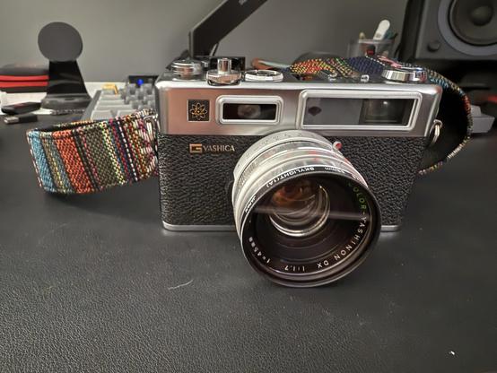 A Yashica electro 35 from the front, with colorful webbed strap visible