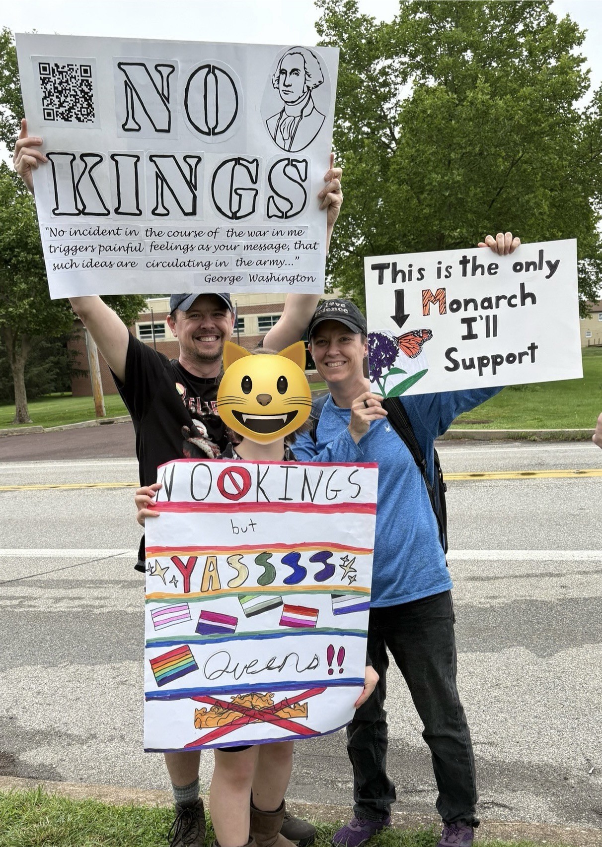 Two individuals are holding colorful protest signs. One sign states "NO KINGS" with a quote from George Washington. The other sign reads, "This is the only Monarch I'll Support," accompanied by a drawing of a butterfly.